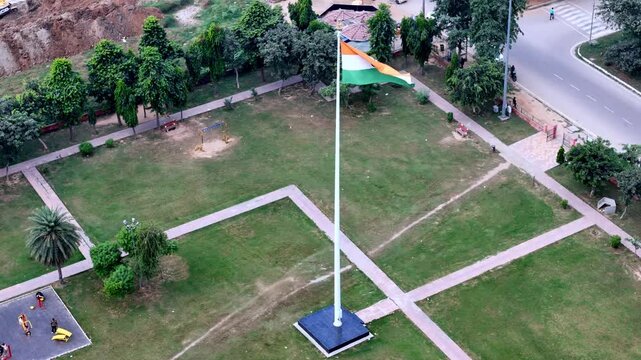 Drone video of India&rsquo;s National Flag standing tall at the heart of a green urban park, framed by walkways, offices, and residential blocks in Greater Noida.
