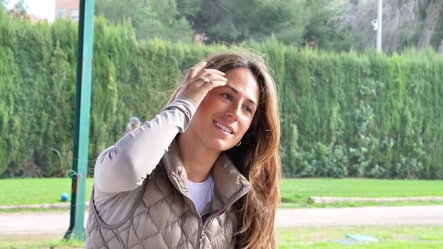 A woman smiles on a golf driving range., wearing a gray jacket and looking to the camera