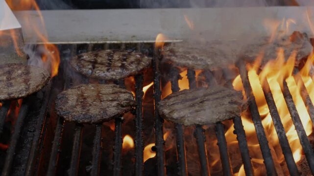 Burgers on greasy smoky charcoal BBQ on summer afternoon on commercial grill in slow motion