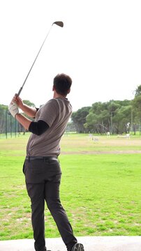 A man is playing golf and swinging his club. Concept of focus and determination as the man prepares to hit the ball. The green grass and the open field create a peaceful and serene atmosphere