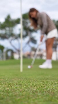 A woman is playing golf and is about to hit the ball with her club. The image is blurry, giving it a sense of motion and action