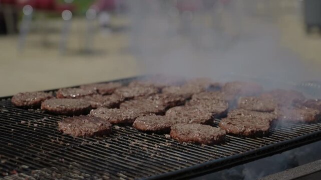 Wide Shot of burgers on greasy smoky charcoal BBQ on a commercial grill summer afternoon tailgate in slow motion