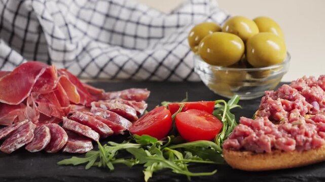 Snack plate. Beef tartare, cherry tomatoes, green olives and fuet sausage, jamon. Wine snack. High quality 4k footage