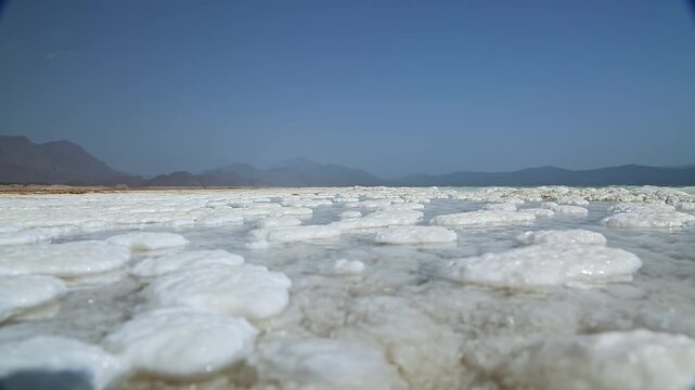 Static shot of salt crystals on the shores of Lake Assal in Djibouti, Africa, white salt crust formations with volcanic mountains in the background, alien-like landscape, 4K 50fps.
