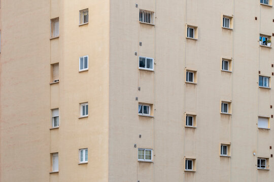 Soft minimal residential facade in Spain with small window grid on beige wall creating calm abstract apartment texture and copy friendly background