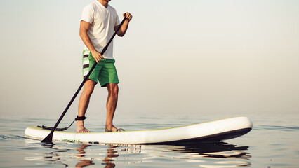 Man stands on paddle board in calm water during early morning hours © fotofabrika