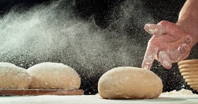 Super slow motion, 1000 fps close-up of baker&rsquo;s hand tossing flour over prepared risen dough on wooden table. Cinematic baking concept, artisan bread preparation and texture detail. Speed ramp effect.