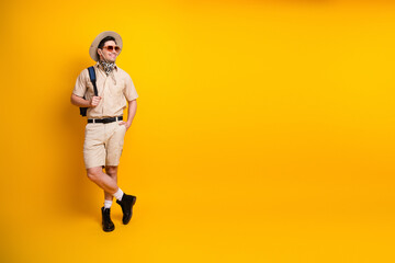 Young man in safari outfit stands against bright yellow wall with hat sunglass backpack ready for travel adventure © deagreez