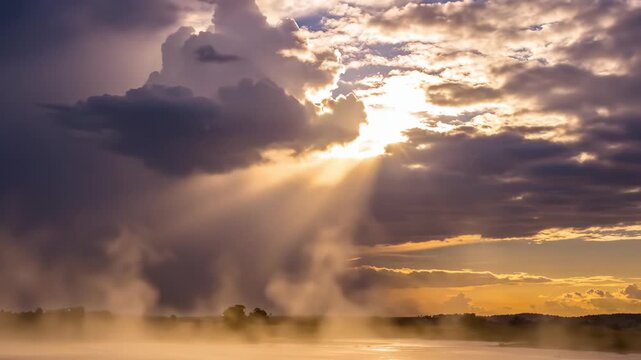 Rays of sun streaming through dramatic storm clouds over a misty, serene water body during a vibrant sunset