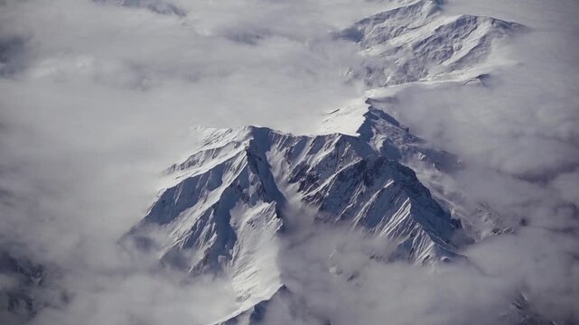 Scenic aerial view of snowy winter mountains from airplane window. Ice mountain range landscape. Majectic high angle view of mountain frozen peaks. Concept of mountaineering and geology.