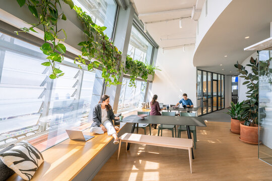 Premium modern coworking in vibrant metropolis: abundant natural light, panoramic skyline views, modular desks, colorful chairs (mint, mustard), plants, lounges, gym rings, social kitchen & young mult
