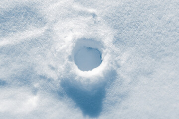 The round hole in the ice, covered with a white fluffy snow background.