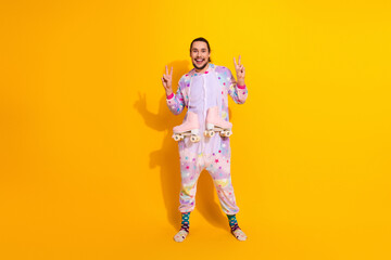 Happy man in pastel pajama jumpsuit holds pink roller skates against a bright yellow background for a playful home party vibe