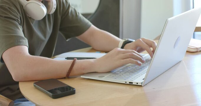 After placing forearms and hovering fingers, man is typing on laptop to complete work near window