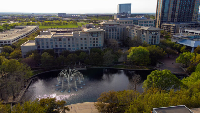 Aerial view of water fountain reflecting sunlight amidst the buildings and greenery, Plano, Texas, United States.