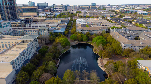 Aerial view of a tranquil pond reflecting the skyline, surrounded by lush greenery and urban architecture, creating a serene oasis in the city, Plano, Texas, United States.