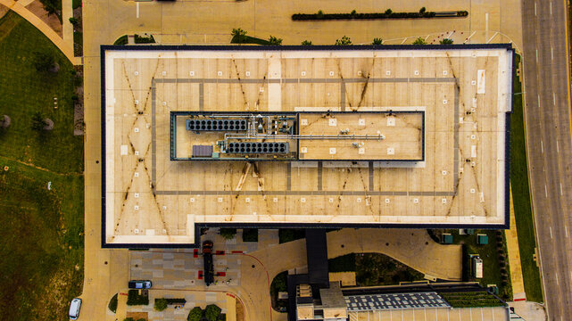 Aerial view of a building with a flat roof, surrounded by greenery and a road with cars, Plano, Texas, United States.