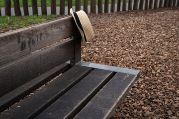 straw hipster summer hat on the back of a wooden park bench outdoors. Simple everyday scene showing a casual personal accessory placed in a public green space.