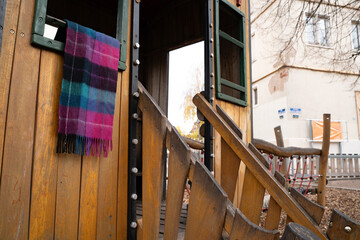 Wool plaid scarf hanging on a small playground house outdoors. Everyday scene showing a personal clothing item left in a public play area, with a casual, real-life feel.