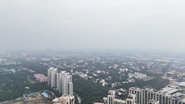 Wide aerial of a modern Indian cityscape wrapped in smog, where mid-rise apartments and buildings cover fade into polluted horizons, reflecting environmental challenges of rapid urban growth.