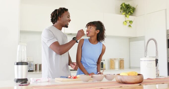 African American couple tasting and prepping fruit at kitchen island cutting board with man feeding