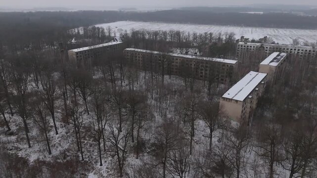 Cinematic drone footage of an abandoned Soviet-era barracks complex near Leipzig, Germany. Snow-covered buildings spread through a quiet forest, creating a calm and atmospheric winter scene.