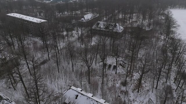 Cinematic drone footage of an abandoned Soviet-era barracks near Leipzig, Germany. Snow-covered buildings lie hidden in a forest, creating a calm and atmospheric winter scene.