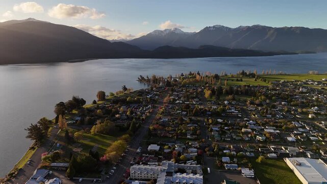 Cinematic 4K 60fps drone flight approaching the town of Te Anau at golden hour, revealing the lakeside community and Fiordland mountains under a sunset sky