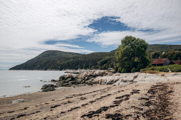 Obraz premium Sandy beach and rocky shoreline with gentle waves along the Saint Lawrence River in rural Quebec village, Port-au-Persil, Canada