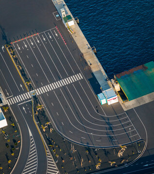 Aerial view of the dark tarmac meeting the deep blue sea at the port, with crisp white markings guiding the way, Playa Blanca, Canary Islands.