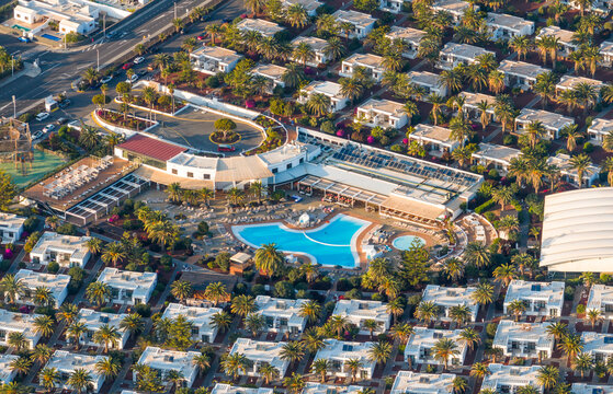 Aerial view of a resort with a vibrant blue pool contrasting against the stark white buildings and lush green palm trees, Playa Blanca, Canary Islands.