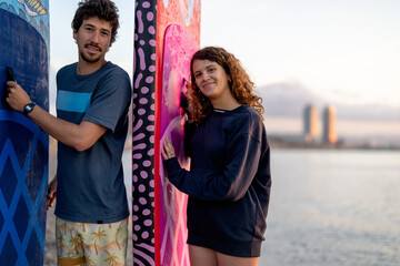Friends share a joyful moment at the beach during sunset, holding vibrant surfboards while laughing