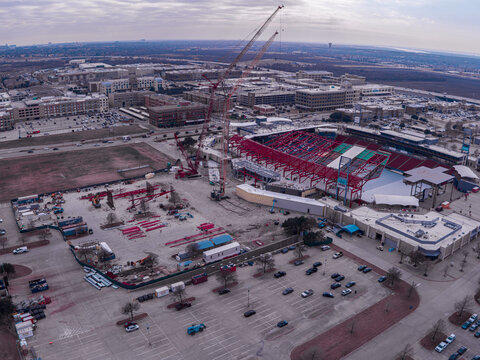 Aerial view of the vibrant red and white stadium contrasting against the pale urban sprawl under a cloudy sky, Frisco, Texas, United States.