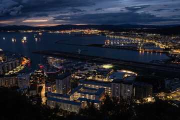 Fototapeta premium A stunning overhead perspective of Gibraltar's compact urban landscape, showcasing the seamless coexistence of sea traffic, air transport, and contemporary coastal development. Real estate market