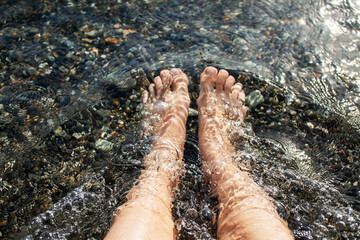 Woman feet in clear sea water over pebbles. Summer beach vacation concept for travel agency advertisement or tourism blog post