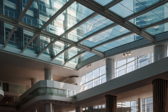 A detailed low-angle view looking through a large glass skylight at a contemporary multi-story office building. The bright interior atrium features white structural columns and reflective glass panels
