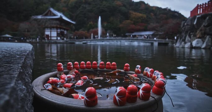 Circle of small daruma dolls on object in pond near Japanese shrine
