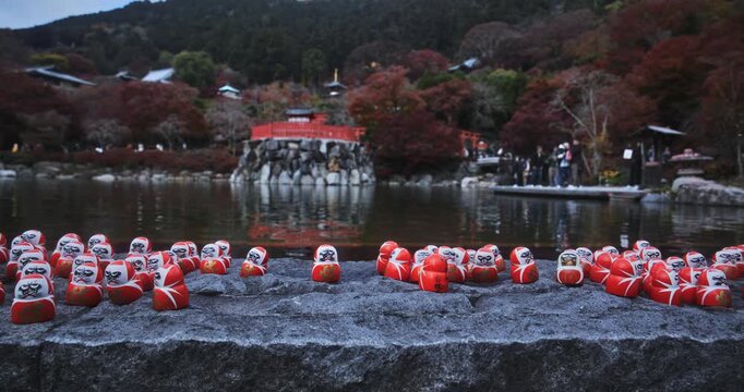 Scattered little daruma dolls on stone area near beautiful Japanese pond