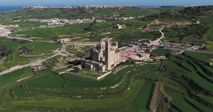 Aerial view of the majestic Ta' Pinu Cathedral standing tall amidst the verdant fields, its intricate architecture a testament to its rich history, Gharb, Ta' Pinu Cathedral, Malta.