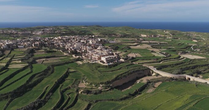 Aerial view of the rural landscape, where green fields contrast with the clustered buildings of Gharb, creating a serene and picturesque scene, Gharb, Malta.