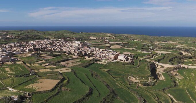 Aerial view of Gharb village surrounded by fields, a tapestry of green contrasting with the terracotta rooftops, Gharb, Ta' Pinu Cathedral, Malta.