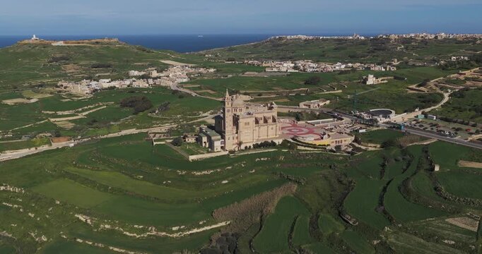 Aerial view of the majestic Ta' Pinu Cathedral rising from the lush green landscape, its intricate architecture contrasting with the surrounding fields, Gharb, Malta.