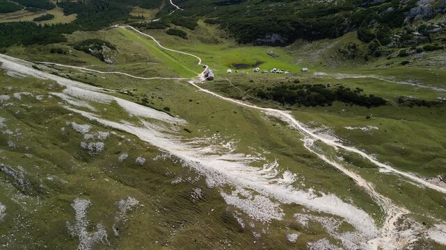 Aerial footage on Sennes Plateau Dolomites South Tyrol Italy, camera lifts from green meadows and limestone slopes to reveal mountain skyline with drifting cumulus clouds
