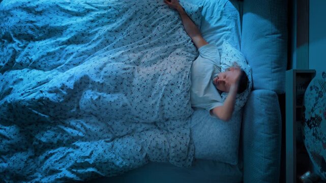 Man is trying to sleep in his bed at night. Insomnia. Tossing and turning in bed because he can't sleep