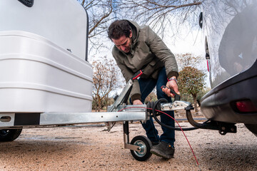 Man connects caravan hitch to vehicle tow ball, preparing for outdoor camping road trip and travel adventure in nature