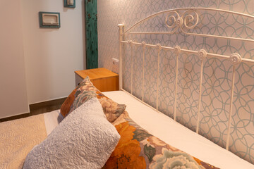 Cozy bedroom featuring a white iron headboard, patterned wallpaper, and floral pillows, creating a comfortable home decor