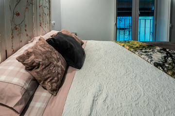 Modern bedroom interior featuring a comfortable bed with pillows, patterned quilt, art headboard, and balcony door