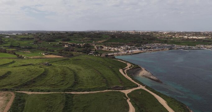 Aerial view of the lush green fields meeting the clear blue sea, with the rugged coastline adding texture, Munxar Path, Marsaskala, Malta.