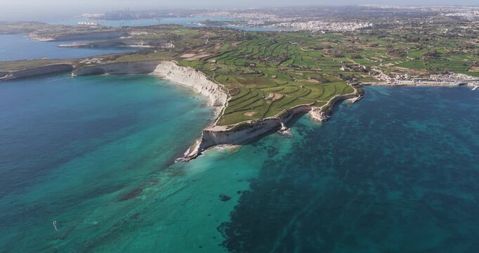 Aerial view of the rugged coastline where the light colored cliffs meet the clear turquoise and dark blue waters, Munxar Path, Marsaskala, Malta.