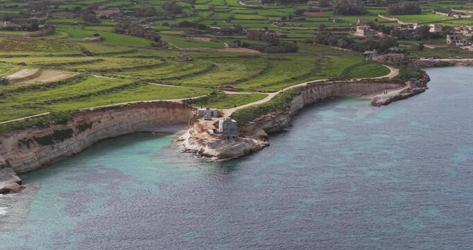 Aerial view of the rugged Munxar Path coastline with its contrasting turquoise waters and green fields, Munxar Path, Marsaskala, Malta.
